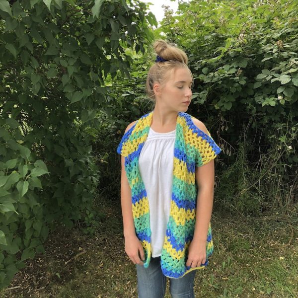 Free crochet pattern: Summer Isle Cardigan by Itchin' for Some Stitchin' in Red Heart Bunches of Hugs yarn for Underground Crafter - woman wearing striped, sleeveless crochet cardigan, standing against greenery